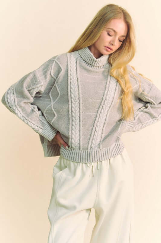 Cozy gray cable-knit turtleneck sweater with dropped shoulders, exuding stylish warmth for colder seasons.