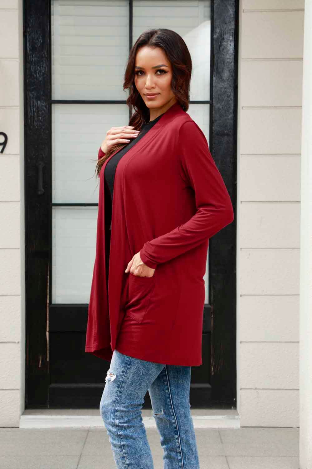 Woman wearing a red open front long sleeve cardigan with pockets over a black top, paired with blue jeans.