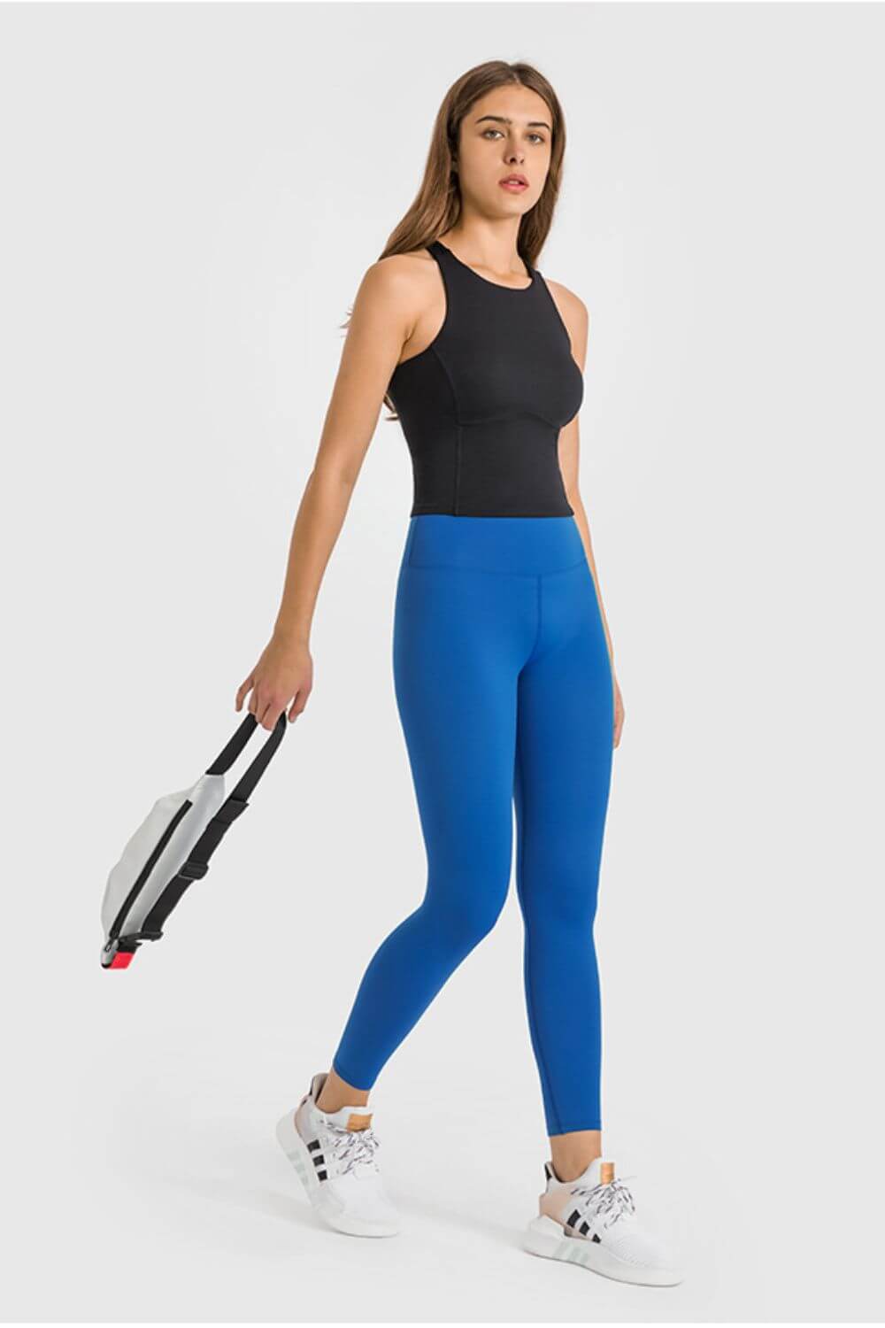 Woman in stylish blue high waist yoga leggings and black top, ready for a workout with a gym bag in hand.