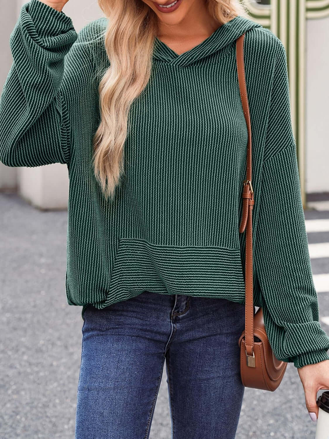 Woman wearing a green textured kangaroo pocket long sleeve hoodie with jeans and a crossbody bag