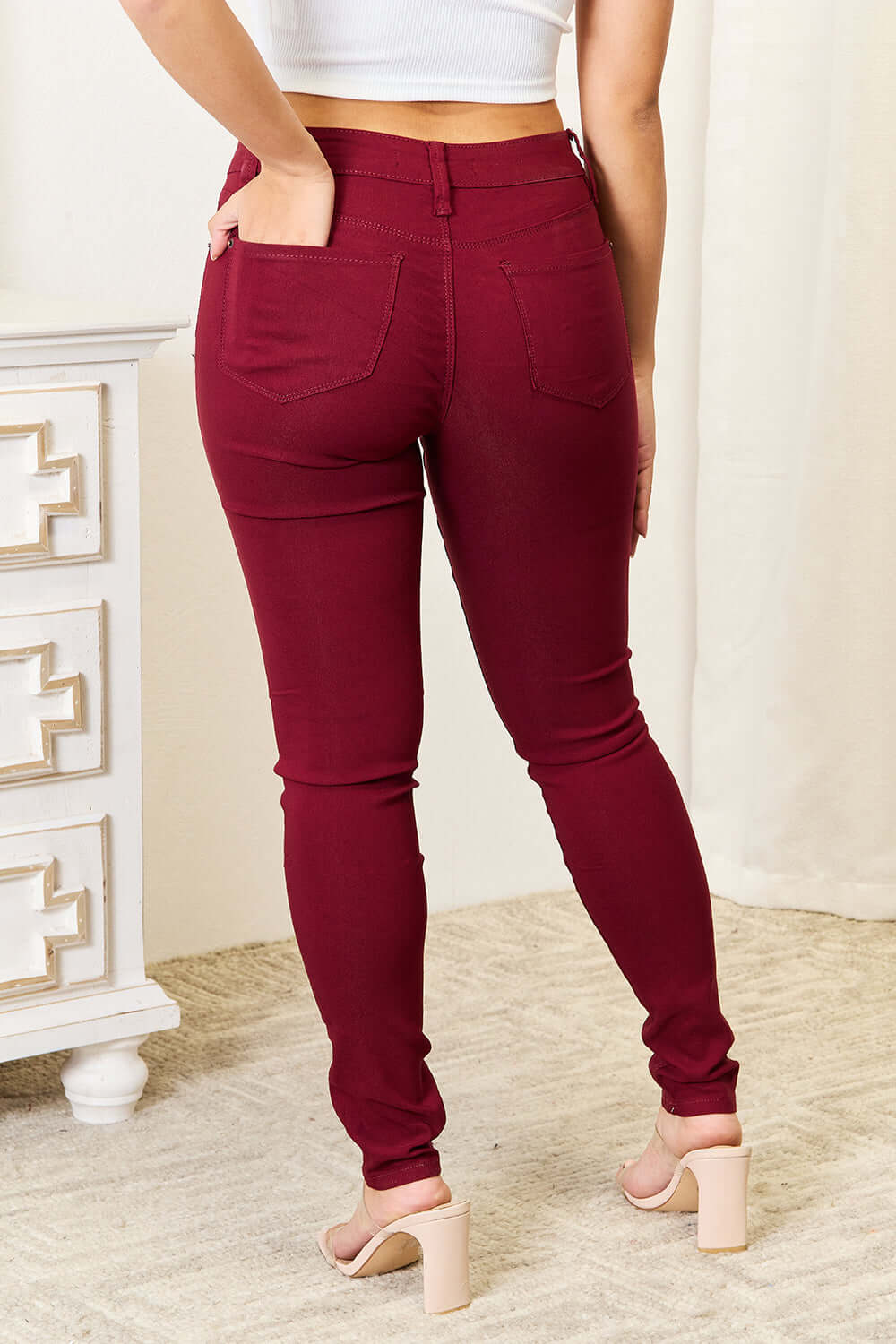 Woman wearing maroon skinny jeans from YMI Jeans, featuring rear pockets and a stretchy, curve-accentuating fit.