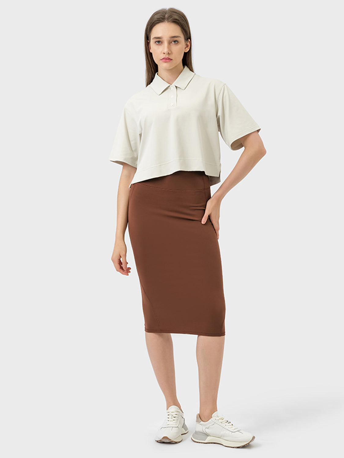 Model showcasing the Millennia Slit Wrap Active Skirt in brown, paired with a stylish cropped shirt and sneakers.