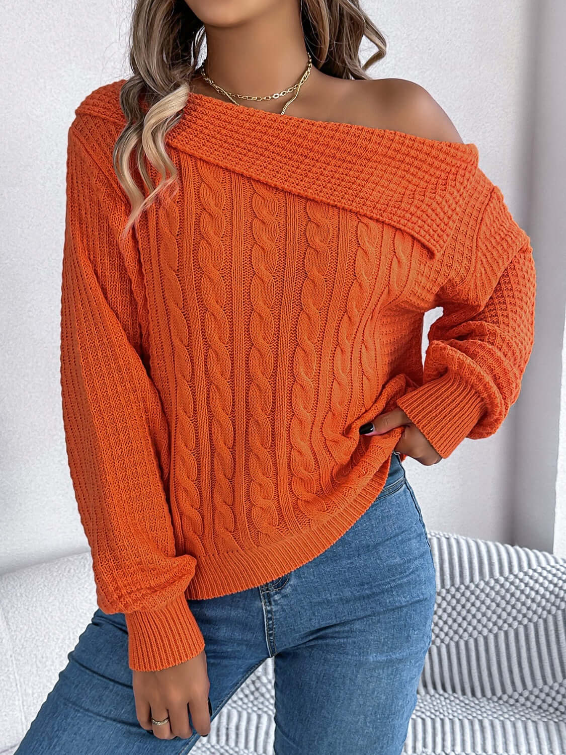 Woman wearing Bella Road Cable-Knit One Shoulder Long Sleeve Sweater in orange paired with blue jeans.