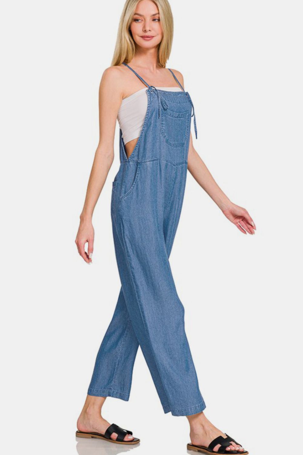 Woman in washed adjustable strap wide leg denim overalls, styled for a casual and chic look.