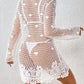 Woman wearing a Cutout Tied V-Neck Long Sleeve Cover-Up in white crochet design over a white bikini, showcasing sheer and stretchy material.