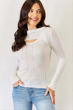 Woman wearing a white fitted long sleeve cutout top with a tank top interior and a shrug-style pullover, paired with blue jeans.