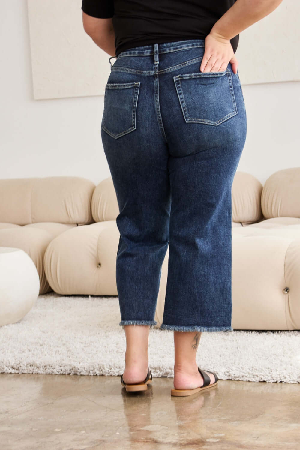 Back view of model wearing high waist raw hem distressed jeans with tummy control in a living room setting.