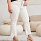 Woman wearing Mini Mia Full Size Tummy Control High Waist Raw Hem Jeans in cream color with wedges, showcasing a stylish and comfortable look