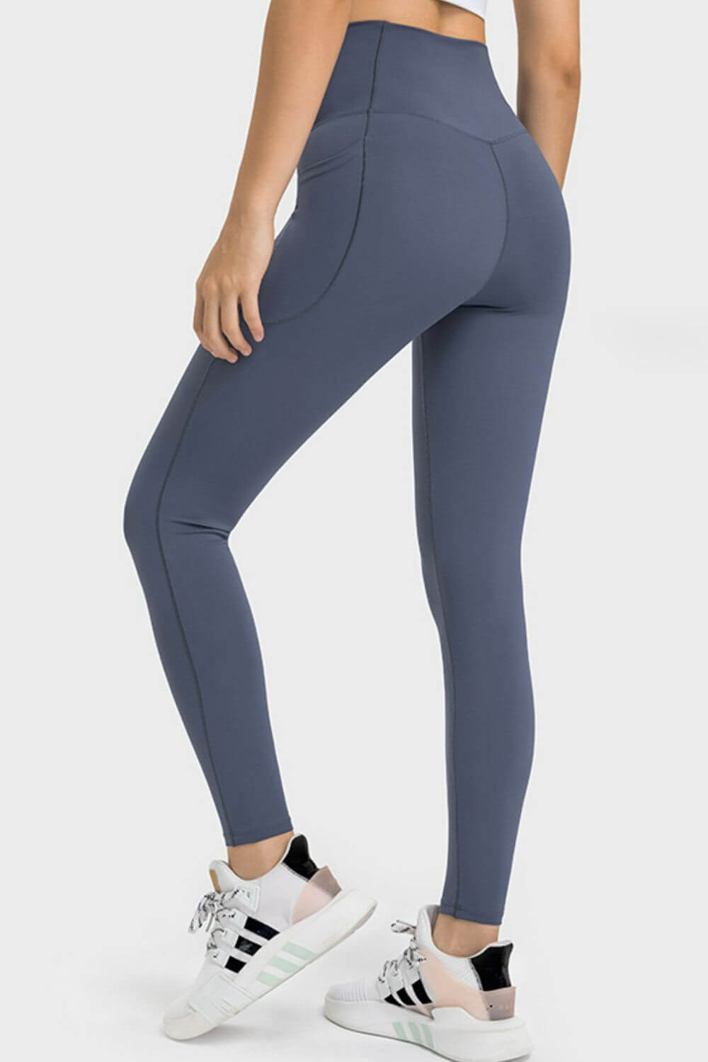 Stylish woman showcasing Millennia V-Waist Yoga Leggings with pockets, rear view in a studio setting.