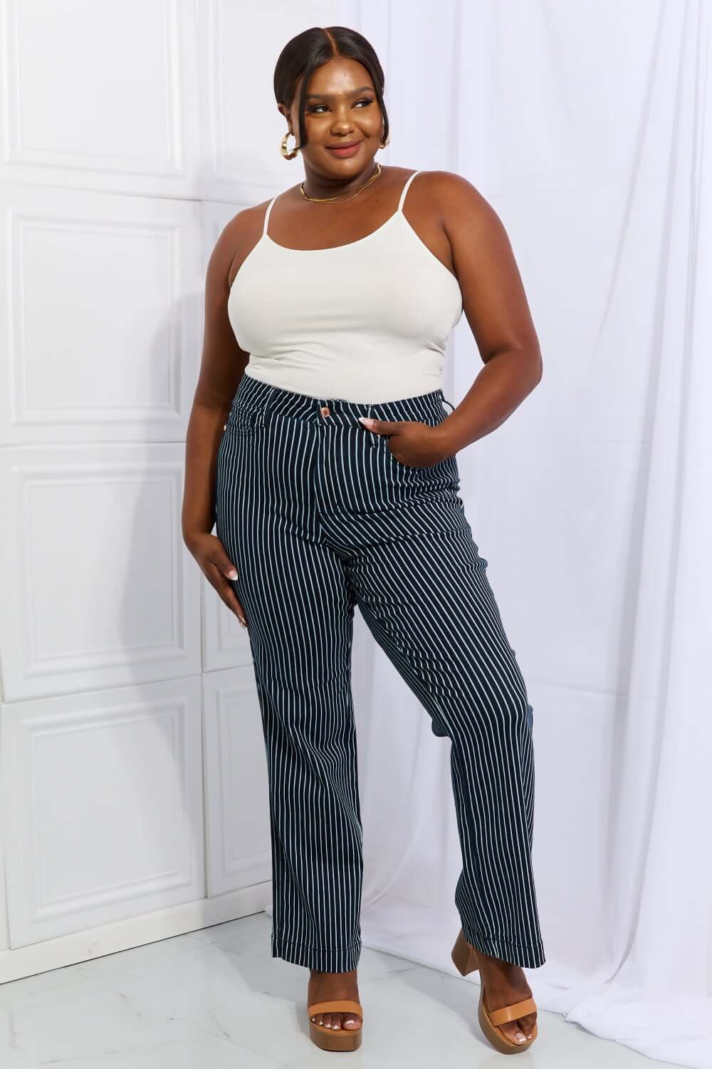 Woman wearing Cassidy Full Size High Waisted Tummy Control Striped Straight Jeans by Judy Blue, posing confidently