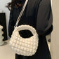 Quilted puffy crossbody bag with removable strap in cream color, worn on shoulder, showcasing versatile fashion design.