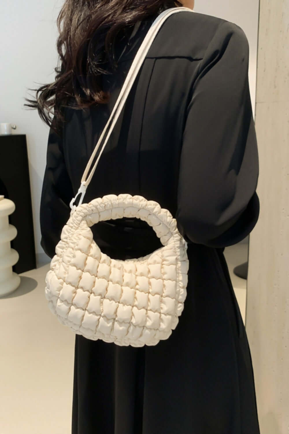 Quilted puffy crossbody bag with removable strap in cream color, worn on shoulder, showcasing versatile fashion design.