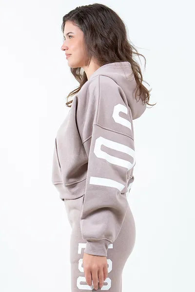 Model showcasing the American Bazi 'Los Angeles' cropped hoodie in beige with graphic detail and drawstring design.