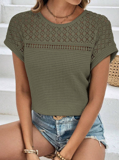 Woman wearing a semi-sheer green waffle-knit round neck short sleeve top with lace detail and denim shorts