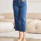 Woman wearing Crop Chloe Full Size Tummy Control High Waist Raw Hem Jeans (RFM Jeans) in living room setting.