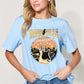 Woman wearing light blue graphic round neck short sleeve T-shirt with "Nashville" print, paired with blue jeans.