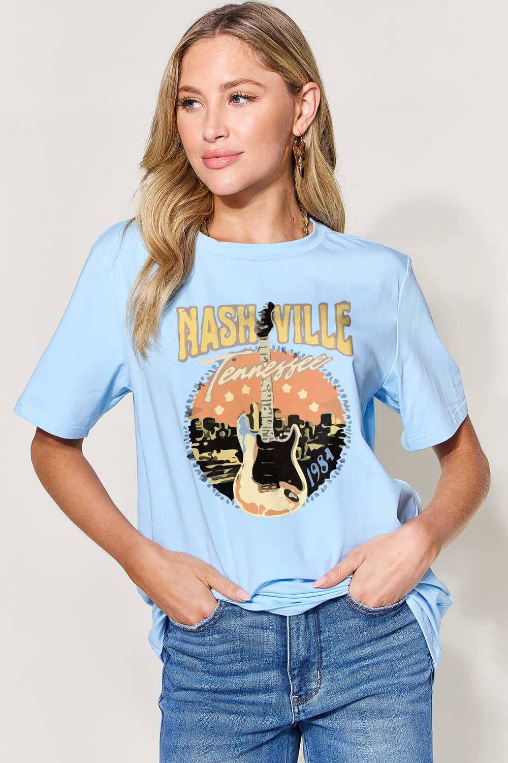 Woman wearing light blue graphic round neck short sleeve T-shirt with "Nashville" print, paired with blue jeans.