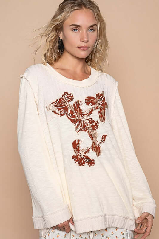 Stylish model wearing an embroidered ivory knit top featuring floral designs, perfect for casual or dressy occasions.