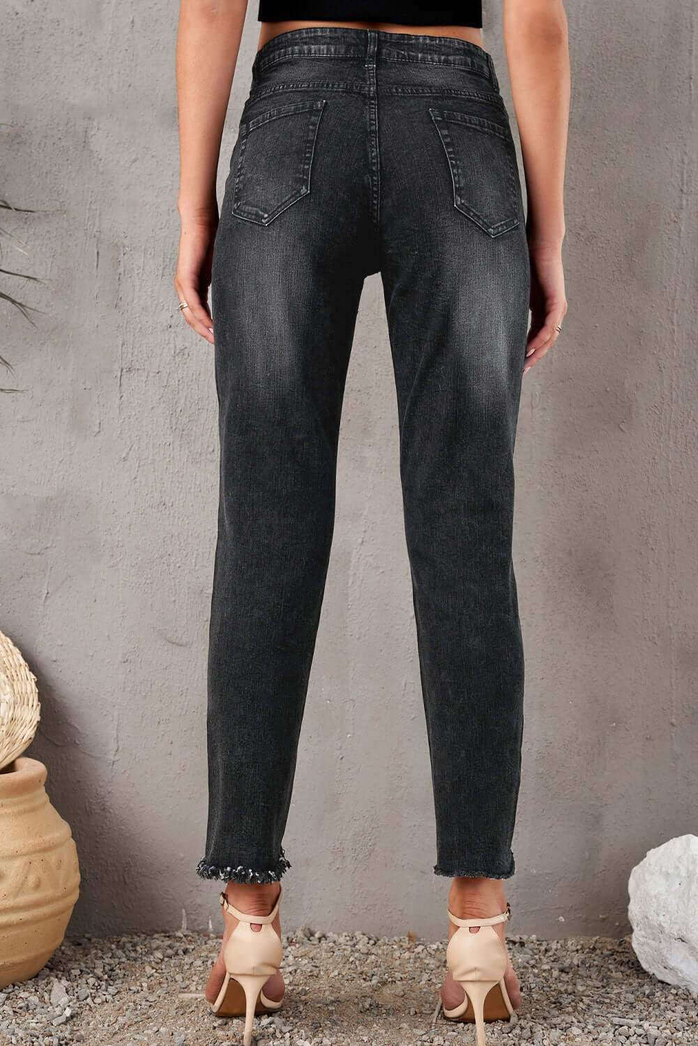 Back view of stylish distressed cropped jeans in black, featuring a slightly stretchy fit, worn by model in a studio setting.