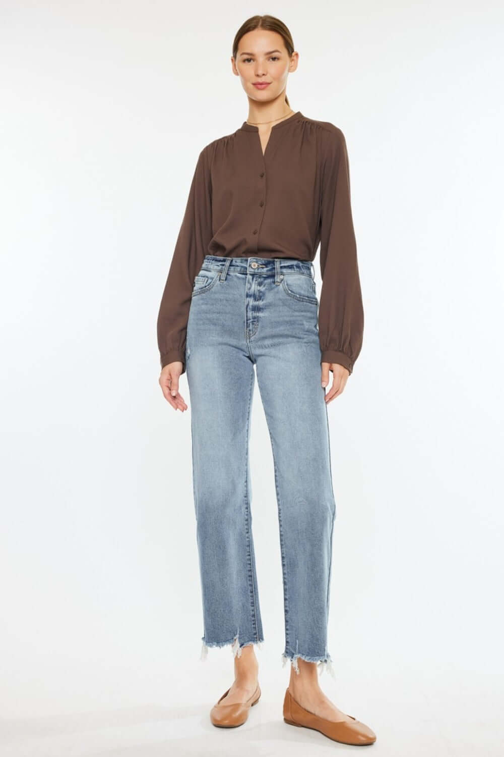 Woman wearing Kancan High Rise Slim Wide Leg Jeans in light wash with stylish hem details, paired with a brown blouse and flats.