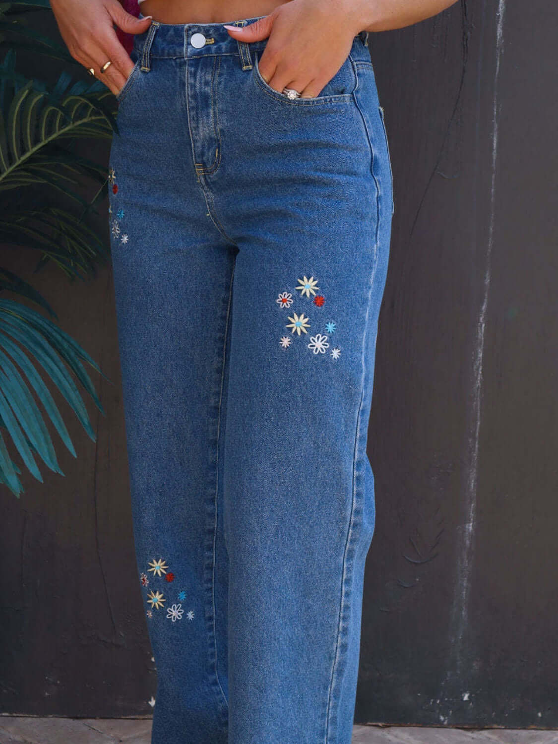 Embroidered straight jeans with pockets featuring floral designs worn by a person, slightly stretchy 100% cotton material.