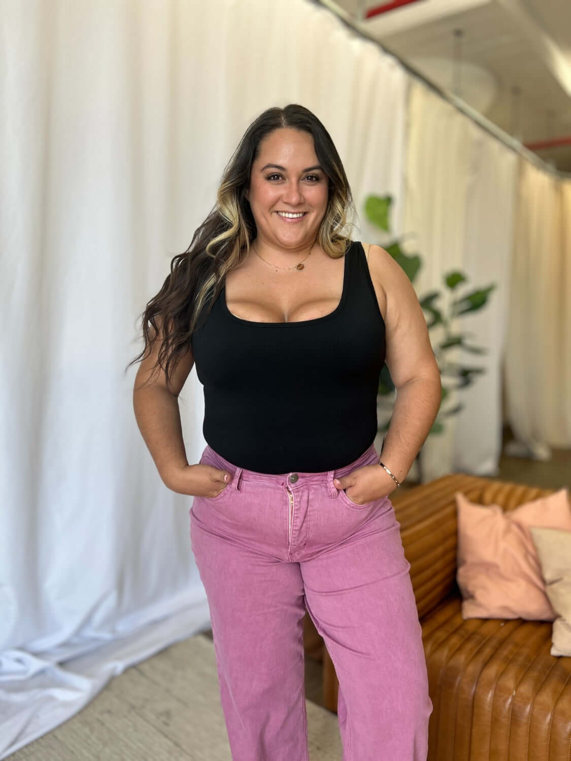 Woman wearing RFM Full Size High Rise Garment Dye Wide Leg Jeans in pink, paired with a black tank top, standing in a stylish room.