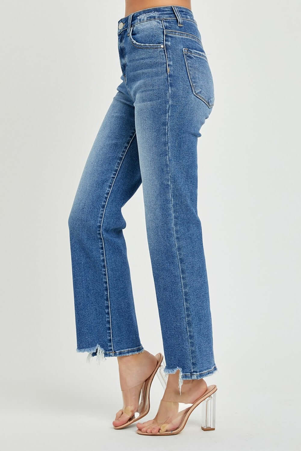 High-rise straight leg jeans with a chic streamlined look, featuring a classic blue wash and frayed hem, paired with clear high heels.