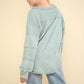 Woman wearing a VERY J Washed V-Neck Exposed Seam Knit Top with drop shoulder design, long sleeves, and raw edge detail in light blue color.