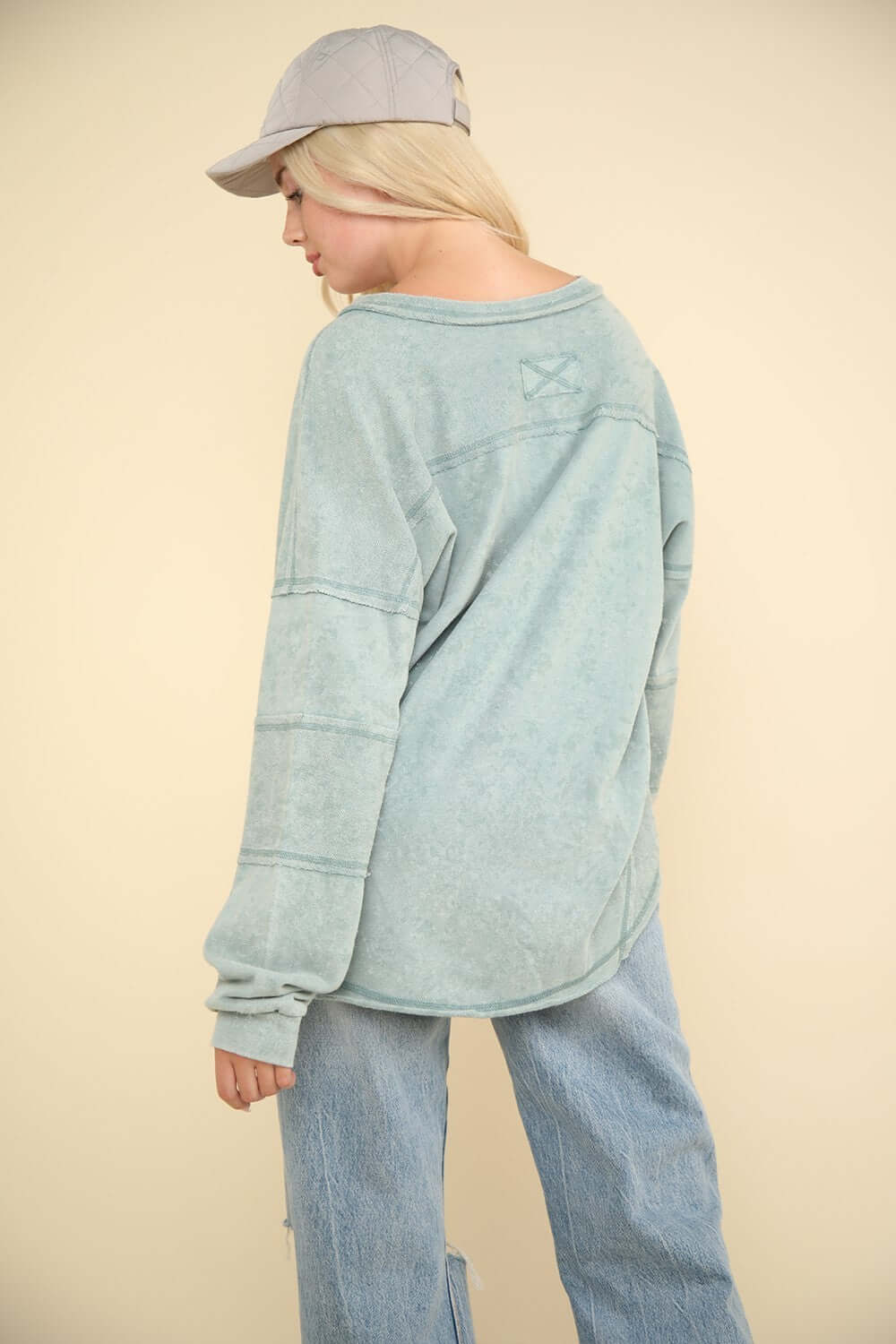 Woman wearing a VERY J Washed V-Neck Exposed Seam Knit Top with drop shoulder design, long sleeves, and raw edge detail in light blue color.