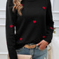 Woman wearing Devine Lace Detail Heart Long Sleeve Sweater with red heart accents, paired with jeans and a beige clutch