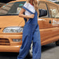 Woman wearing Bella Road Wide Leg Denim Overalls next to a yellow van, showcasing wide straps and stylish comfort.