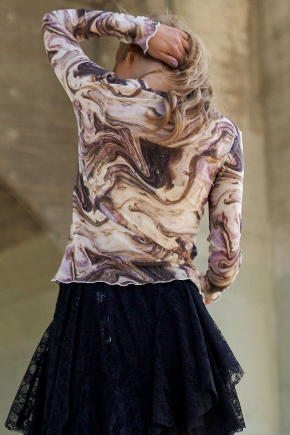 Woman wearing a marble design long sleeve mesh top with elegant swirls and black lace skirt, showcasing contemporary style.