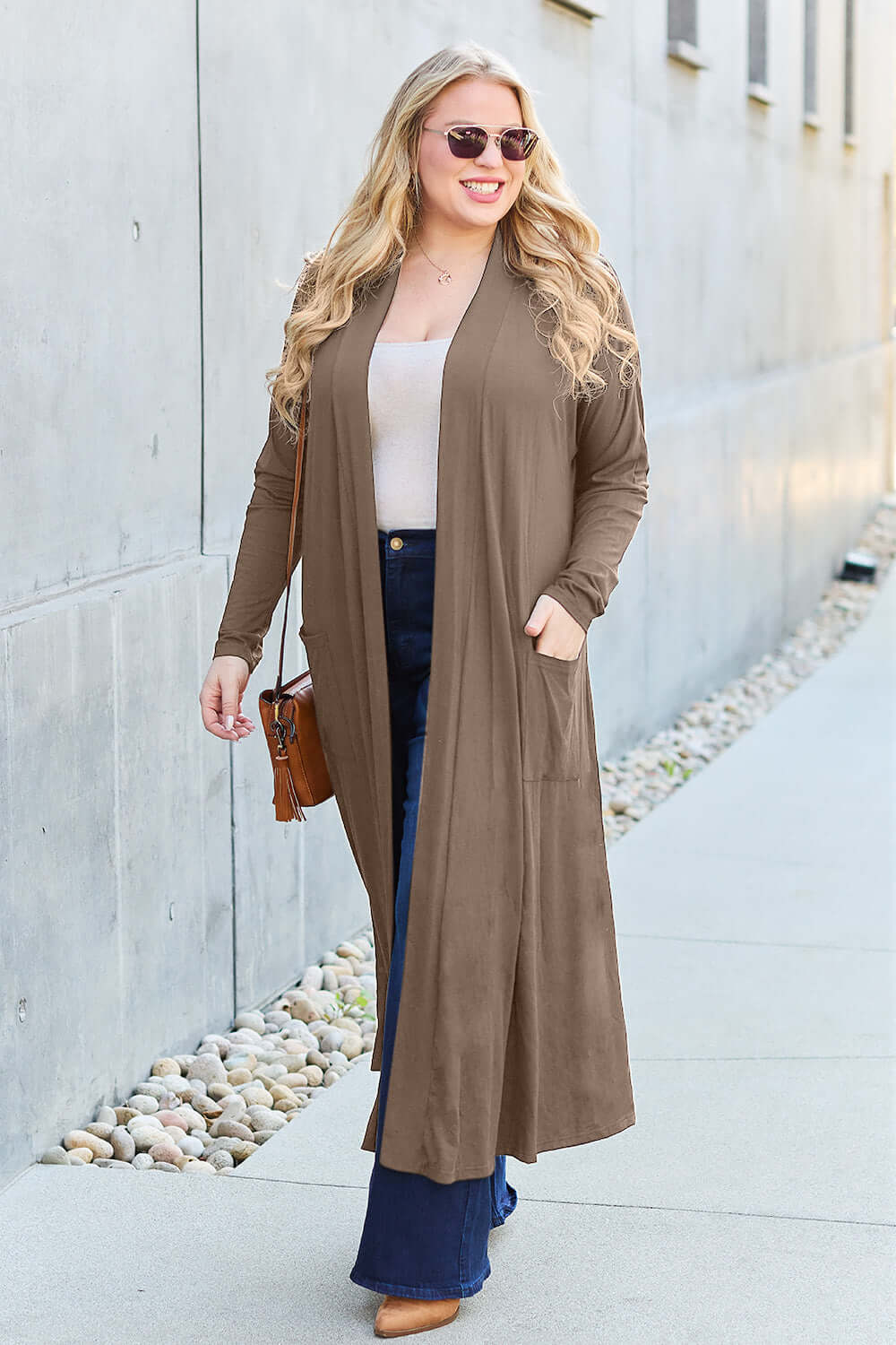 Woman wearing an open front long sleeve cover-up with pockets, paired with jeans and a handbag, walking outdoors.