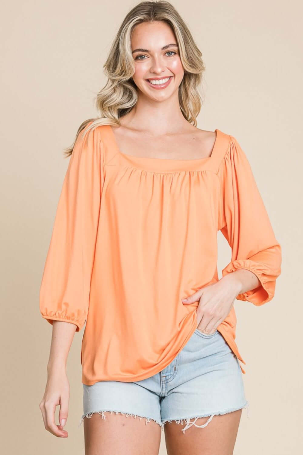 Woman wearing a stylish Square Neck Puff Sleeve Top in orange with light denim shorts, showcasing a chic and modern fashion look.