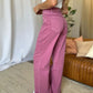 Woman wearing RFM Full Size High Rise Garment Dye Wide Leg Jeans in rich pink color, standing in a stylish living room setting.