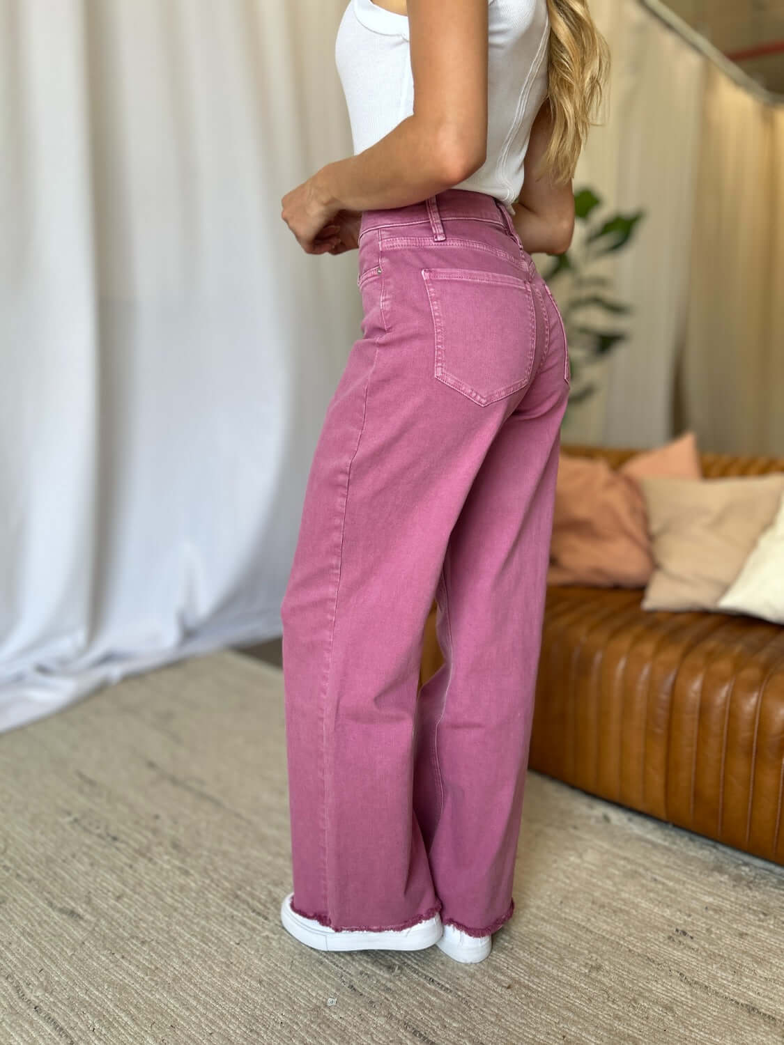 Woman wearing RFM Full Size High Rise Garment Dye Wide Leg Jeans in rich pink color, standing in a stylish living room setting.