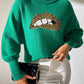 Woman wearing green Bella Road Lip Turtleneck Sweater with leopard print lips, styled with white pants and black quilted purse.