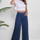 Woman wearing stylish wide leg jeans with pockets, white crop top, and white sneakers, showcasing casual chic style.