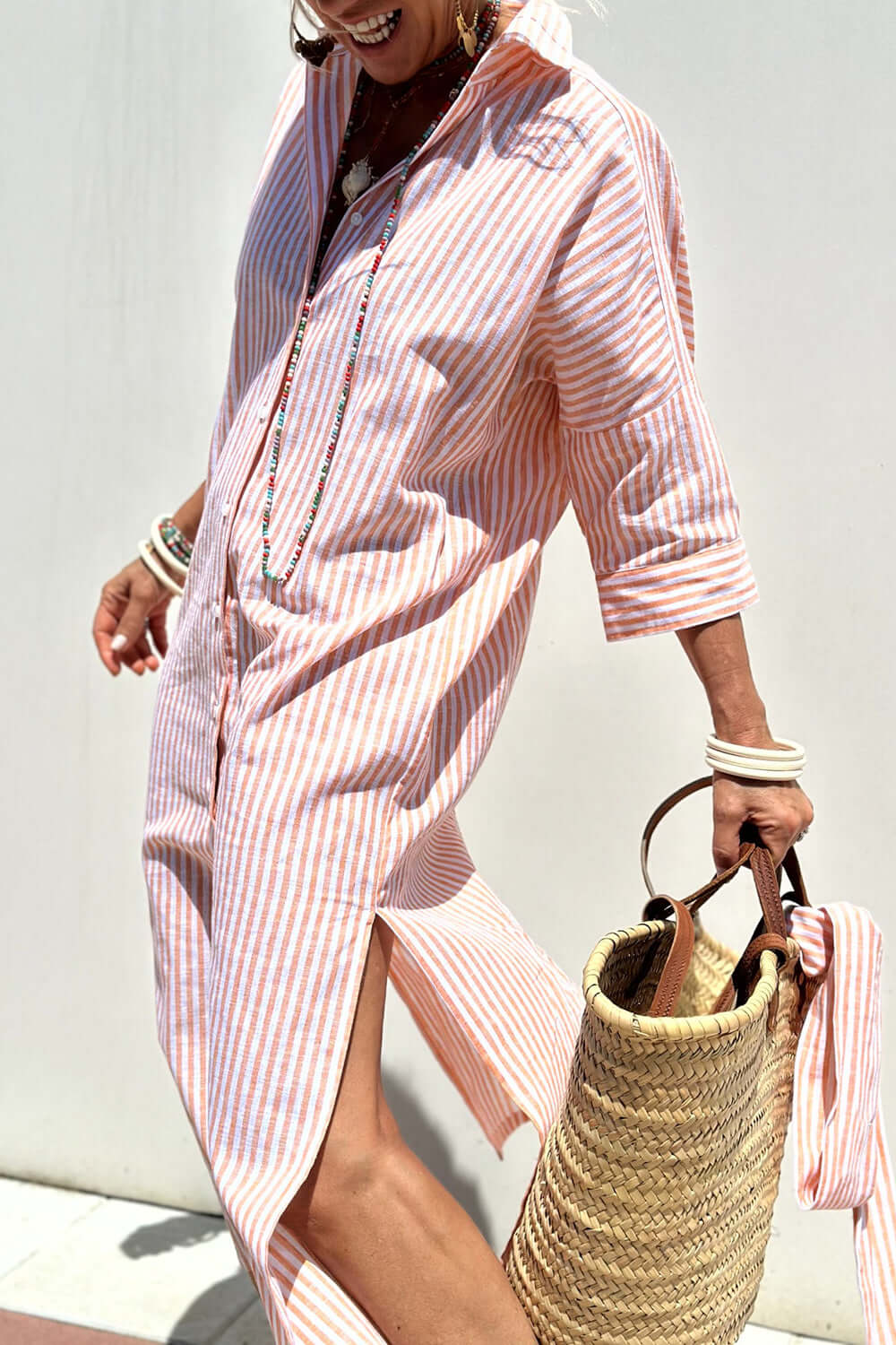 Woman wearing Bella Road Tied Button Up Three-Quarter Sleeve Dress, holding a woven bag, and smiling in the sunlight