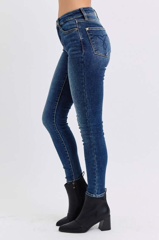 Side view of Judy Blue mid-rise skinny jeans in blue with pockets, styled with chic black ankle boots.