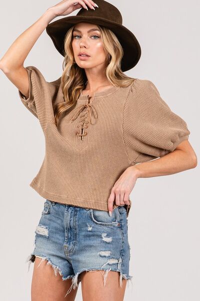 Model wearing SAGE+FIG lace-up waffle knit crop top with distressed shorts and a hat, showcasing trendy casual style.