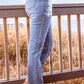 Woman wearing stylish distressed cropped jeans standing barefoot on a wooden deck by the beach.