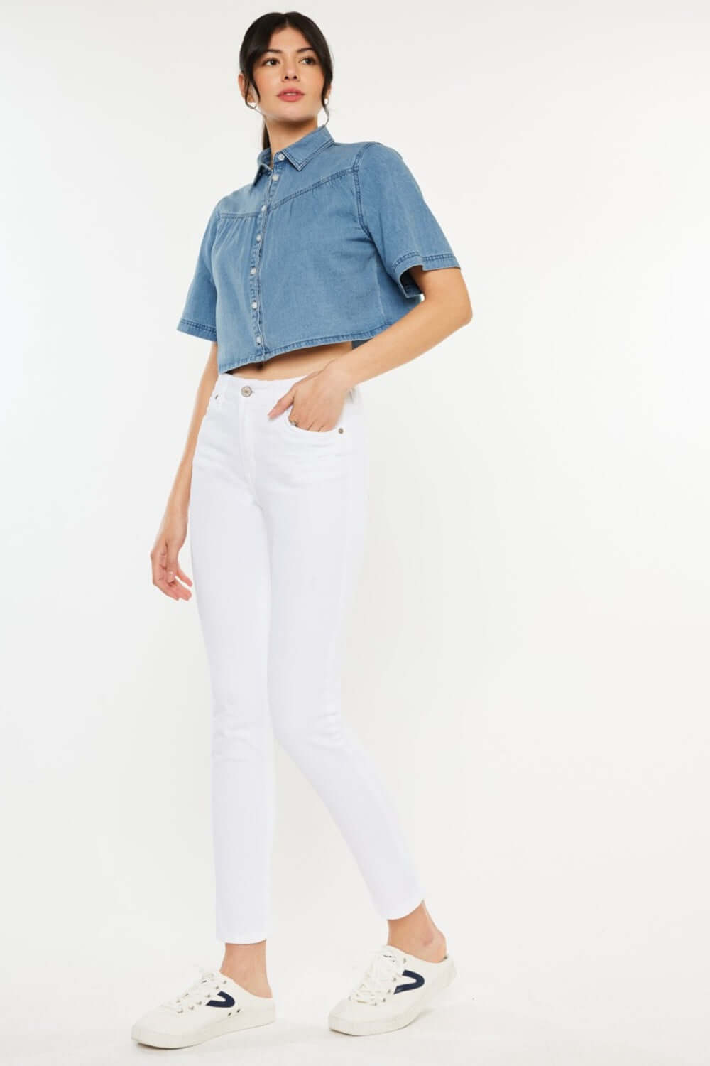 Woman wearing white high rise ankle skinny jeans paired with a blue cropped shirt and white sneakers.