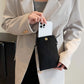 Woman holding Bella Road Suede Snap Down Crossbody Bag with a smartphone inside, wearing a beige blazer.