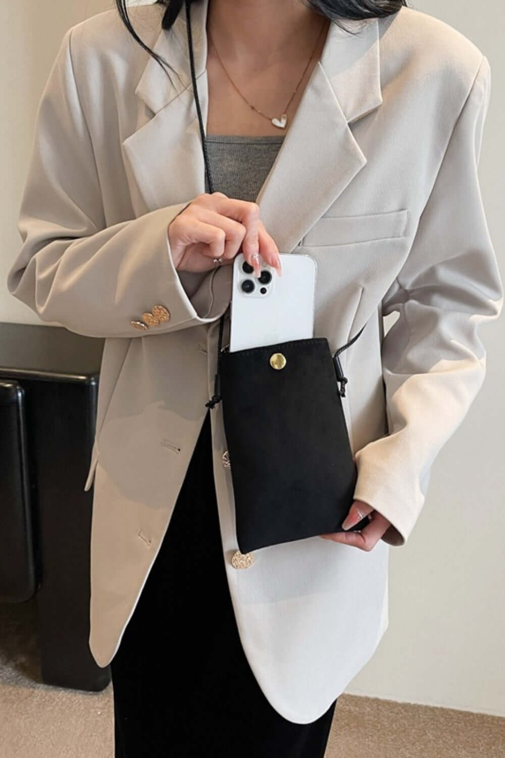 Woman holding Bella Road Suede Snap Down Crossbody Bag with a smartphone inside, wearing a beige blazer.