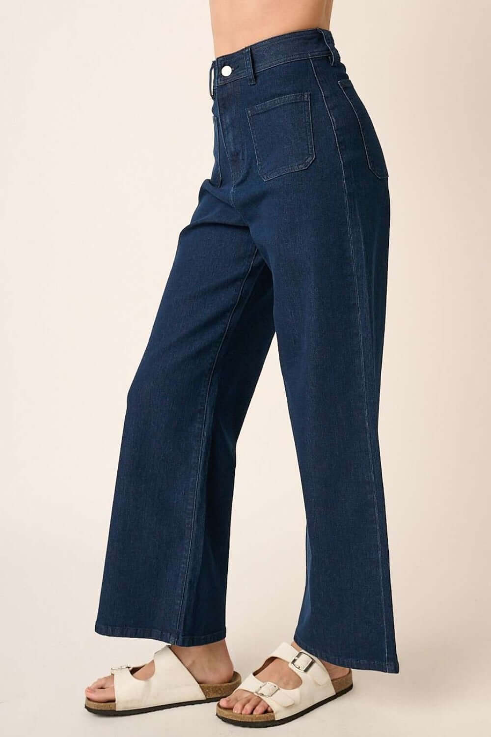 High-waisted wide leg jeans made from soft denim knit, featuring patch pockets, zip fly closure, paired with white sandals.