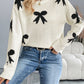 Woman wearing Perfee Bow Graphic Round Neck Long Sleeve Sweater in white with black bow design, paired with jeans for a cozy look.