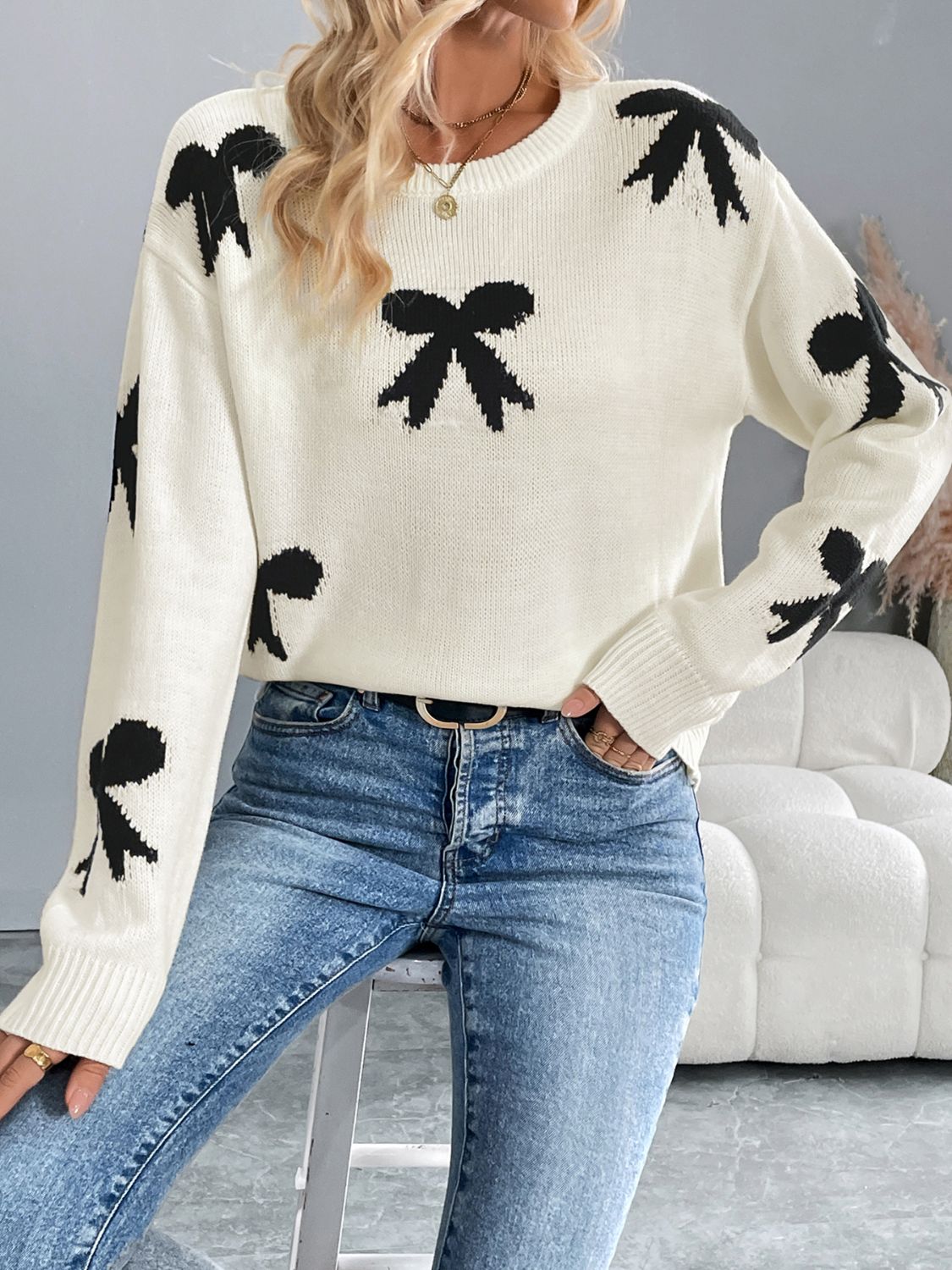 Woman wearing Perfee Bow Graphic Round Neck Long Sleeve Sweater in white with black bow design, paired with jeans for a cozy look.