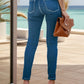 Rear view of woman wearing buttoned skinny jeans with pockets, holding a tan clutch, standing on a terrace by the sea.