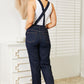 Woman wearing high waist classic denim overalls by Judy Blue Jeans, showcasing a flattering back view in a stylish indoor setting.